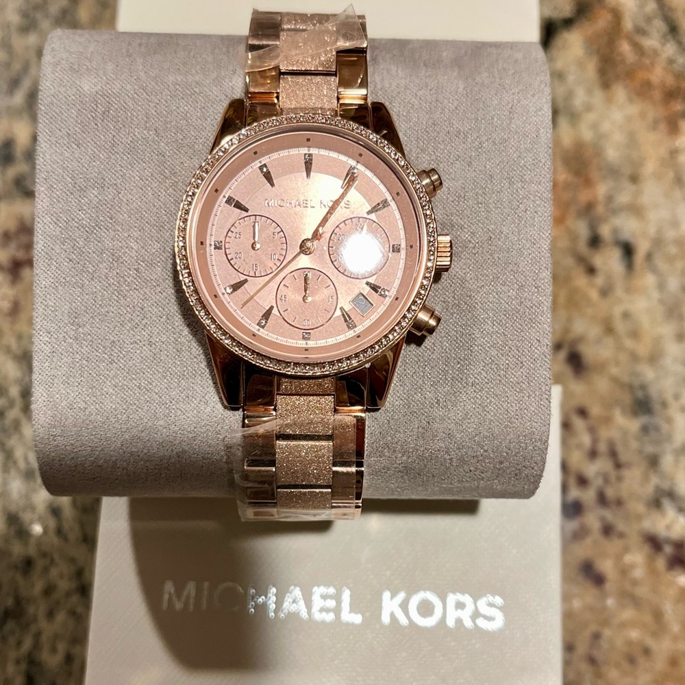 Rose gold with stones around the face. Brand new in a box with film on the band.